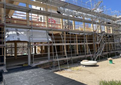 Der Holzbau im Erdgeschoss ist - mit Ausnahme der Fassade - abgeschlossen. Anders als bei den Obergeschossen, wo die Fassadenteile bereits mit eingebauten Fenstern auf die Baustelle geliefert werden, erfolgt im Erdgeschoss die Montage der Fenster vor Ort. - Über ein Entwässerungsrohr wird gerade Regenwasser aus dem 1. OG abgeleitet.