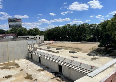 Hinter den Sporthallen wird ein Sportplatz entstehen. Darunter ist eine sog. Rigole eingebaut. Regenwasser wird hier zwischengespeichert und kontrolliert dem Grundwasser zugeführt, statt es über Abwasserkanäle abzuleiten. - Von der Mensa (Bildmitte hinten) stehen bislang nur die Technikräume - rechts wird sich der Speisesaal anschließen.