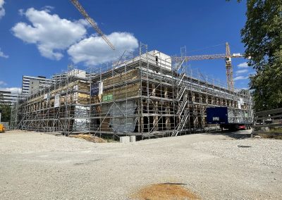 Blick von Südwesten auf das künftige MBG-Schulhaus. Der Holzbau ist mittlerweile im 1. Obergeschoss angekommen. In etwa vier Wochen folgt hier zum Abschluss die Außenfassade, wobei die Fassadenteile bereits mit Fenstern angeliefert werden.